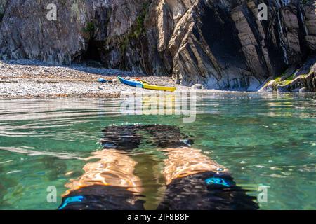 Un kayakiste nageant dans la mer avec kayak sur la plage, Pembrokeshire, pays de Galles Banque D'Images