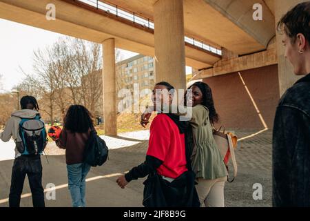 Vue latérale des amis multiraciaux joyeux qui marchent ensemble sous le pont