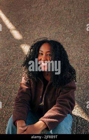 Portrait d'une jeune femme souriante aux cheveux bouclés assis au bord de la route Banque D'Images