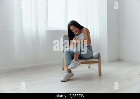 Crampes orteil cassé os cassé dans la jambe. Souffrance tourmentée bronzée belle jeune femme asiatique touche la jambe à la maison intérieur salon. Blessures faibles Banque D'Images