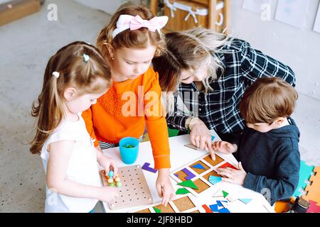 Petits enfants avec un éducateur pliant des détails colorés du constructeur sur le bureau dans la salle de jeux de la vue d'en haut. Jeu intéressant pour les jardins d'enfants en développement Banque D'Images