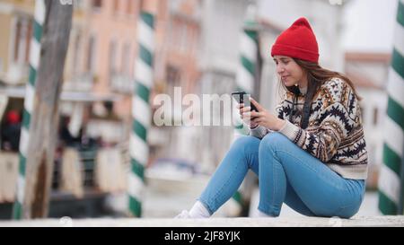 Une jeune femme s'assoit près du front de mer et regarde dans le téléphone dans les rues de Venise Banque D'Images