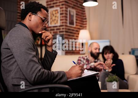 Thérapeute frustré prenant des notes sur papier à la séance de thérapie de couple avec des partenaires mariés, ayant des conflits de relations et des difficultés. Essayer de résoudre des problèmes avec des conseils de psychologie. Banque D'Images