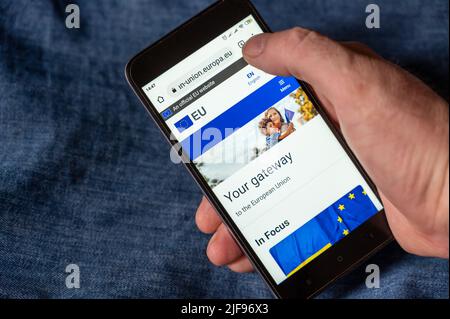 Page d'accueil de l'Union européenne. Page Web officielle sur l'écran de votre smartphone. La main d'un homme maintient le téléphone contre le tissu bleu denim. Ukraine, myko Banque D'Images