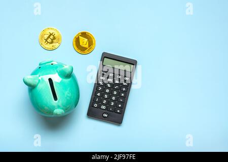 Banque de piggy, calculatrice et pièces de Bitcoin d'or, Ethereum isolé sur fond bleu accumulation de crypto-monnaie, investissement dans le marché de la crypto, concept d'affaires Top View Flat Lay. Banque D'Images