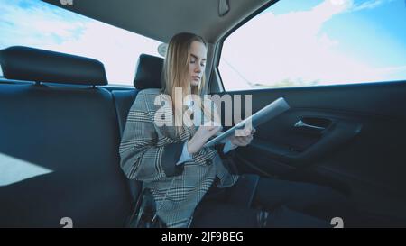 Étudiant occupé travaillant avec sa tablette et son téléphone dans sa voiture. Banque D'Images