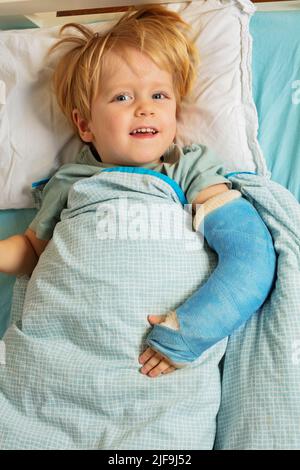 Garçon blond dans le lit d'hôpital avec plâtre moulé sur la main cassée Banque D'Images