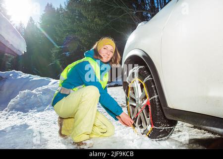 Femme mettant des chaînes d'hiver sur la roue de voiture pour la chaussée glacée Banque D'Images