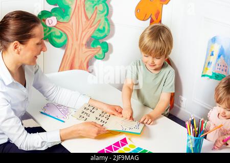 La femme enseigne aux petits enfants à lire des lettres dans le livre Banque D'Images