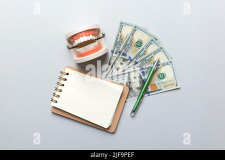 Composition de pose à plat avec modèle de typographie dentaire pédagogique et argent avec carnet sur table colorée, vue de dessus. Traitement coûteux. Banque D'Images