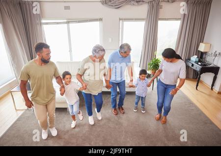 Famille de race mixte s'amusant et dansant dans le salon à la maison. Petits garçons et grands-parents ayant une journée de plaisir à la maison avec leurs parents. Ayant Banque D'Images