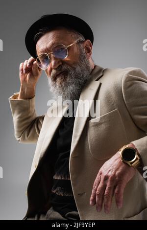 portrait d'un homme âgé barbu dans une élégante veste beige et un chapeau derby sur fond gris Banque D'Images