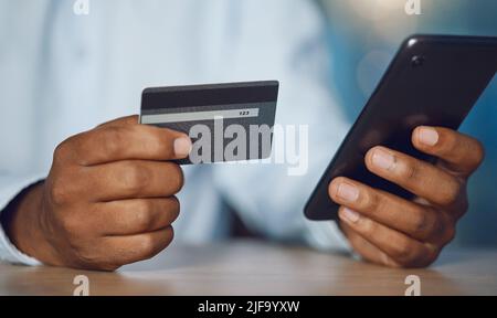 Gros plan mains de l'homme africain utilisant un téléphone tout en tenant sa carte de crédit. Homme d'affaires afro-américain magasiner en ligne tout en travaillant tard la nuit à Banque D'Images