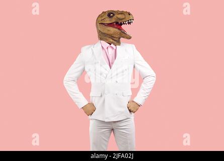 Portrait d'un homme dans un drôle masque de dinosaure et un costume blanc debout sur un fond rose Banque D'Images