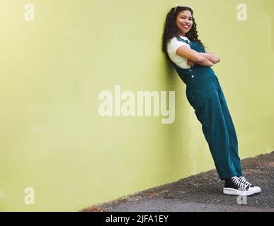 Fullbody belle course mixte de mode femme souriant avec ses bras croisés contre un fond de mur vert lime dans la ville. Jeune femme hispanique heureuse Banque D'Images