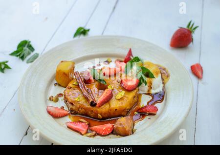 Tranche d'ananas caramélisée avec crème glacée, fraises, pistaches, menthe et bâton de cannelle Banque D'Images