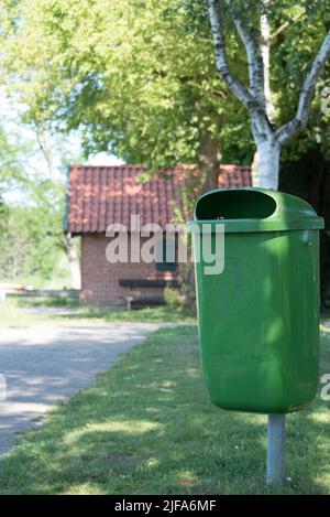 vider la poubelle verte à herbe ou la poubelle avec un pictogramme à côté d'un chemin avec un bouleau et une petite maison en briques à l'arrière Banque D'Images