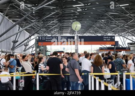 30 juin 2022, Rhénanie-du-Nord-Westphalie, Köln/Bonn : les voyageurs aériens attendent de longues files d'attente devant les comptoirs d'enregistrement à l'aéroport de Cologne/Bonn. L'aéroport de Cologne/Bonn avait déjà signalé de longs délais d'attente devant les postes de contrôle de sécurité. Les voyageurs doivent se rendre à l'aéroport au moins 2,5 heures avant le départ. Photo: Thomas Banneyer/dpa Banque D'Images