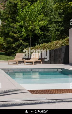 Vue verticale sur la piscine dans le jardin de la maison avec chaises longues en bois et obturateur de piscine en été Banque D'Images