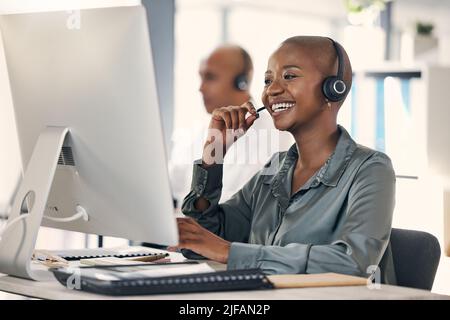 Un jeune agent de télémarketing de centre d'appels afro-américain satisfait parlant sur un micro-casque tout en travaillant sur un ordinateur dans un bureau. Femme confiante et amicale Banque D'Images