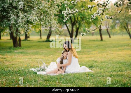 Une jeune femme heureuse s'assoit sur une couverture de pique-nique et encroise sa fille. Pique-nique d'été de la mère et de la fille dans le verger de pomme. Banque D'Images