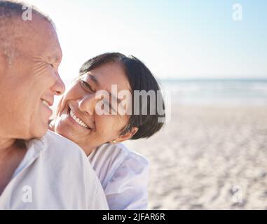 Couple de race mixte affectueux et mature partageant un moment intime sur la plage. Un mari et une femme de haut niveau qui profitent d'une journée d'été au bord de la mer. Ils aiment Banque D'Images