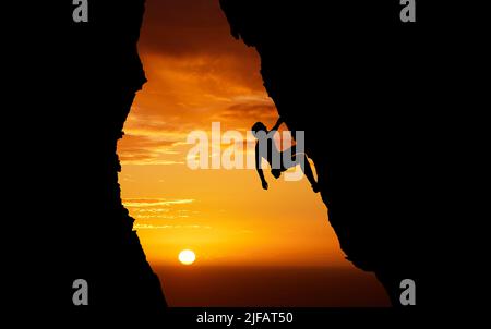 Des sensations fortes méconnues pour les sports extrêmes. Homme inconnu faisant de l'escalade au coucher du soleil. Photo sombre d'un jeune homme passionné par lui Banque D'Images