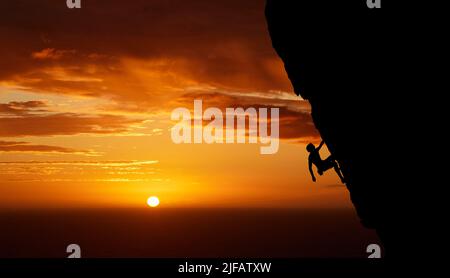 Des sensations fortes méconnues pour les sports extrêmes. Homme inconnu faisant de l'escalade au coucher du soleil. Photo sombre d'un jeune homme passionné par lui Banque D'Images