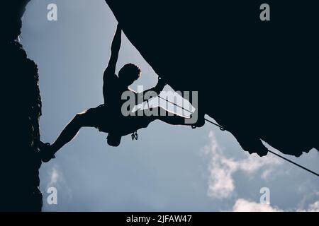 Des sensations fortes méconnues pour les sports extrêmes. Inconnu homme faisant de l'escalade de montagne . Photo sombre d'un jeune homme passionné par sa forme physique Banque D'Images