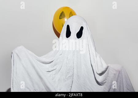 Joyeux Halloween. Un enfant dans un costume fantôme blanc fait maison et des boules orange peintes. Design festif, concept de fête. Fête de la Toussaint. Banque D'Images