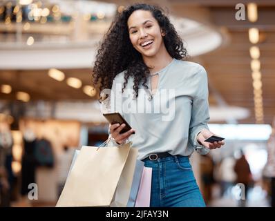Portrait belle femme de course mixte debout avec son téléphone et sa carte de crédit tout en faisant du shopping dans un centre commercial. Jeune femme hispanique portant des sacs, dépense Banque D'Images