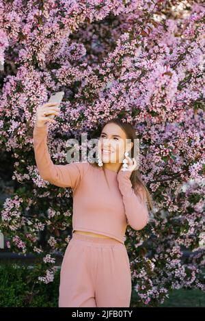 Une jeune femme prend un selfie sur son téléphone entouré de pommiers roses. Saison de printemps Banque D'Images