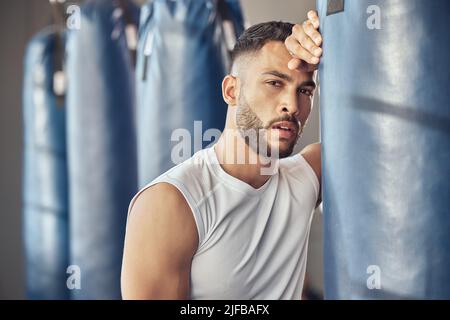 Portrait d'un boxeur fatigué appuyé sur un sac de poinçonnage. Un combattant mma épuisé se reposant après un entraînement dans la salle de gym. Routine de boxe bodybuilder dans la salle de gym. Fort Banque D'Images