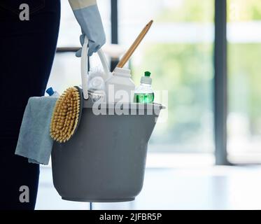 Une femme inconnue de race mixte tenant des fournitures de nettoyage tout en nettoyant son appartement. Un nettoyant domestique non reconnaissable portant des gants de nettoyage en latex Banque D'Images