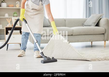 Un travailleur domestique inconnu qui soulève et nettoie sous un tapis. Une race mixte femelle non reconnaissable utilisant un aspirateur sous un tapis pour commencer Banque D'Images