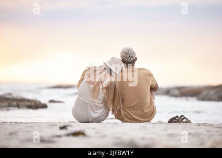 Vue arrière d'un jeune couple faisant une pause à la plage pendant le coucher du soleil. Une femme de race blanche et son petit ami mixte se détendant et appréciant la vue à Banque D'Images
