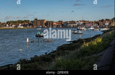 Port et marina de Wells-à-côté-de-la-mer en soirée, à la lumière de Beach Road, à travers East Fleet, avec une skene d'oies silhouettés contre un ciel bleu. Banque D'Images