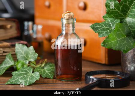 Bouteille de sirop de feuilles de lierre ou teinture de toux. Bouteille d'extrait de feuilles d'Ivy et armoire de médecine en bois avec remèdes apothécaire, vieux livres sur fond. A Banque D'Images