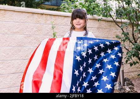 Fille à cheveux noirs tenant et agitant un drapeau des États-Unis, dans le jardin de sa maison. Concept de célébration, jour de l'indépendance, Etats-Unis d'Amer Banque D'Images