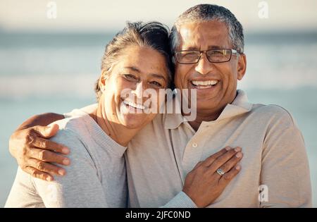 Portrait en gros plan d'un couple de course mixte et affectueux, debout sur la plage et souriant pendant le coucher du soleil à l'extérieur. Couple hispanique montrant l'amour Banque D'Images
