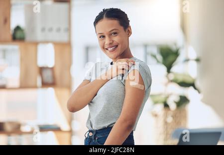 Jeune heureuse femme de race mixte montrant un bandaid sur son bras après avoir reçu un vaccin Covid. Portrait d'une femme hispanique confiante souriant tout en montrant Banque D'Images