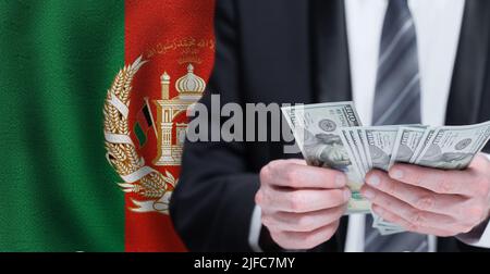 Des mains tenant de l'argent en dollars sur le drapeau de l'Afghanistan Banque D'Images