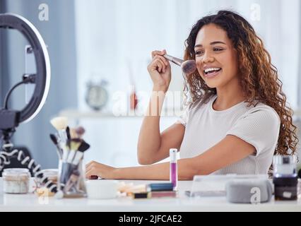 Une femme hispanique enregistrant un tutoriel de maquillage pour son blog de beauté avec son téléphone tout en étant assis à la maison. Influenceur afro-américain vit Banque D'Images