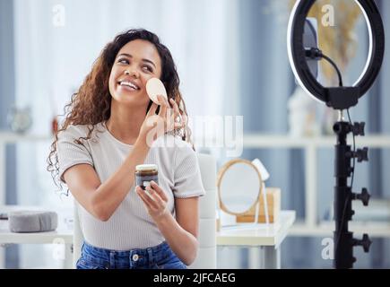 Une femme hispanique enregistrant un tutoriel de maquillage pour son blog de beauté avec son téléphone tout en étant assis à la maison. Influenceur afro-américain vit Banque D'Images