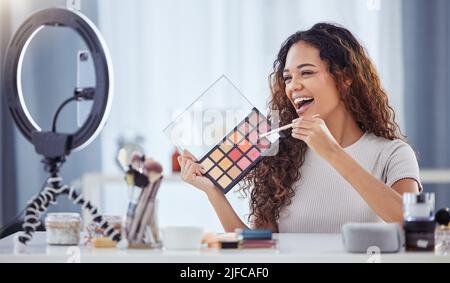 Une femme hispanique enregistrant un tutoriel de maquillage pour son blog de beauté avec son téléphone tout en étant assis à la maison. Influenceur afro-américain vit Banque D'Images