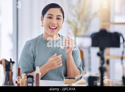 Une belle jeune femme mixte de course qui parle dans un studio à domicile et tient un rouleau facial en quartz rose tout en utilisant un appareil photo pour vlog une routine de soin de la peau Banque D'Images