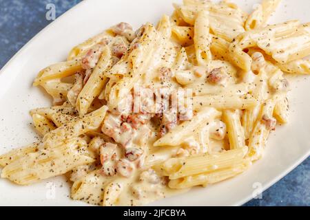 Un gros plan de penne carbonara au jambon, à la sauce crémeuse et aux épices sur une assiette plate Banque D'Images