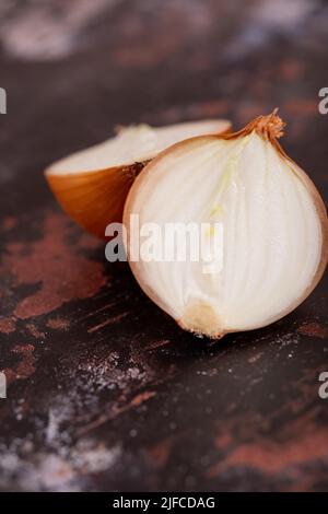 Un oignon blanc divisé en deux avec la peau, sur un fond noir de surface métallique. Banque D'Images