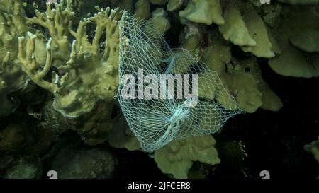 Les articles de cuisine en plastique mis au rebut pendent du récif de corail. Pollution plastique de l'océan. Sac en plastique en maille accroché à un magnifique corail Banque D'Images