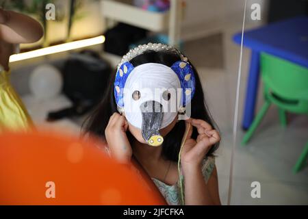 Une petite fille portant un masque en papier coloré à l'avant de son visage est isolée dans le fond de la salle de classe avec un ballon orange. PAP éléphant Banque D'Images